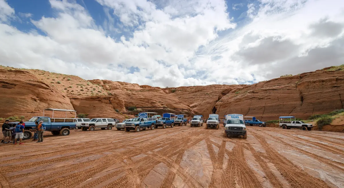 Tourfahrzeuge parken in einem sandigen Wash vor dem Eingang zum Antelope Canyon