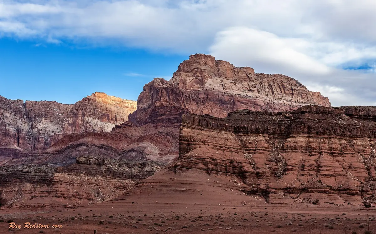 Geschichtete rote und violette Felsen der Vermilion Cliffs unter blauem Himmel mit Wolken